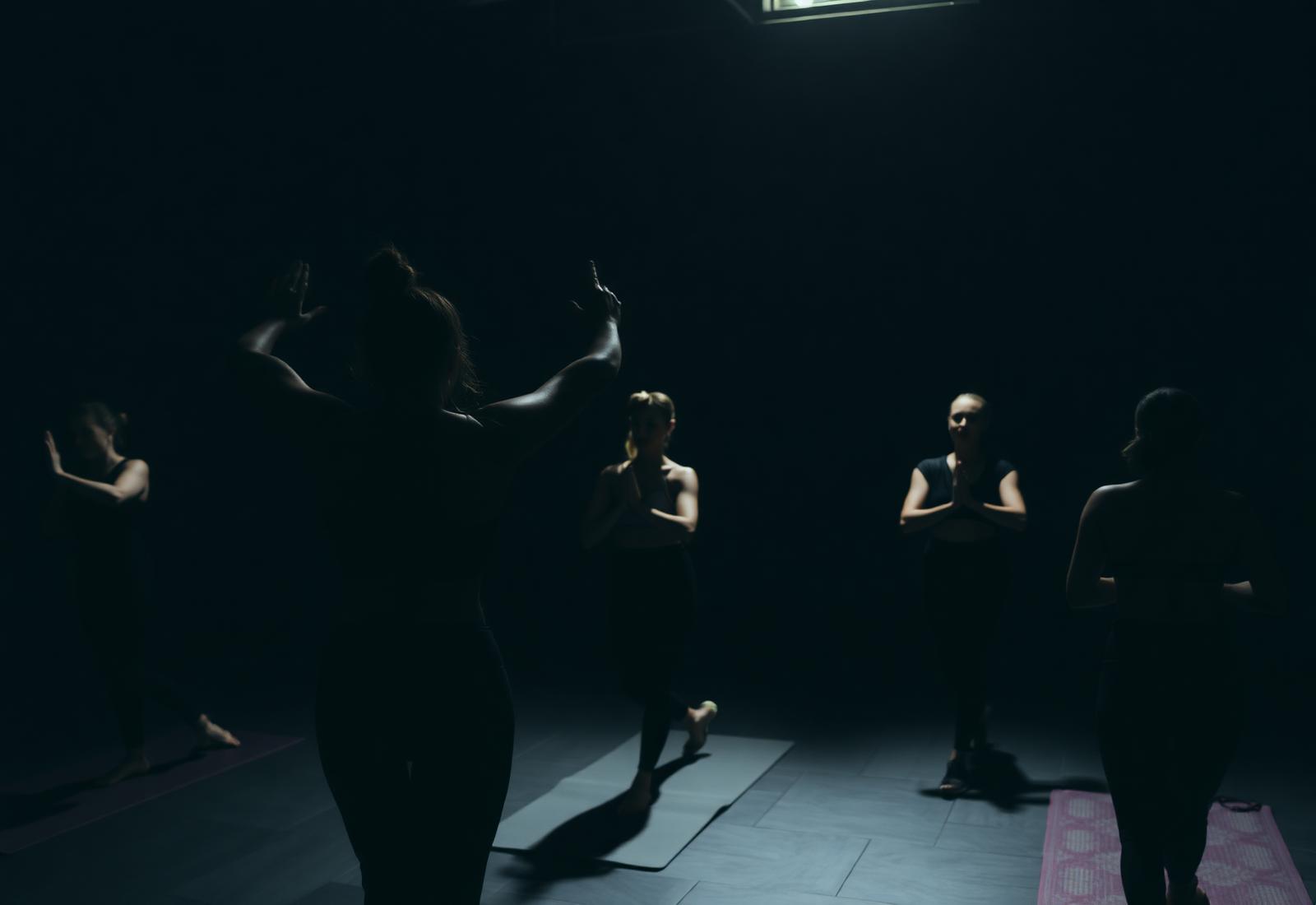 A group of women moving through a yoga class in a dim studio.